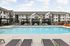 Beautiful apartment complex with a sparkling swimming pool and elegant lounge chairs set against a backdrop of modern architecture.