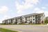 Modern apartment complex with charming architecture, surrounded by greenery, set under a bright blue sky.
