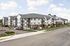 Modern apartment complex with elegant architecture, featuring spacious balconies and ample parking, surrounded by a well-maintained landscape under a bright blue sky.