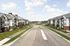 Modern apartment buildings with elegant architectural design overlooking a wide, peaceful street under a bright blue sky.