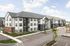 Modern apartment complex with sleek design, surrounded by ample parking and landscaped greenery under a clear blue sky.