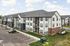 Modern apartment complex with sleek architecture, ample parking, and lush landscaping under a bright blue sky.