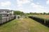 Charming fenced outdoor area adjacent to a modern apartment complex, offering open views of lush green fields and a serene sky, ideal for relaxation and leisure.