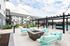 Charming apartment exterior featuring a stylish communal patio with turquoise seating, a cozy fire pit, and string lighting under a clear sky.