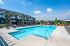 Luxurious apartment complex with a sparkling outdoor swimming pool, modern lounge chairs, and beautifully landscaped surroundings.