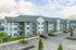 Modern apartment complex with white siding, spacious balconies, and ample parking in a serene suburban setting.