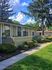 Charming apartment exterior with manicured shrubs and a cozy pathway, surrounded by lush greenery under a bright blue sky.