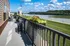 Charming balcony overlooking serene river views with lush greenery, featuring modern black patio furniture and vibrant flower arrangements.