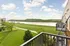 Charming riverside balcony view with lush green landscape, serene water, and rolling hills under a beautiful sky.