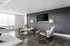 Modern living space with sleek wooden floors, cozy armchairs, and a flat-screen TV. Abundant natural light floods through large windows, creating an inviting atmosphere.