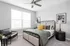 Elegant and bright bedroom with modern decor, featuring a cozy bed with colorful pillows, stylish black chair, and a large window for natural light.