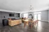 Elegant open-plan living and dining area featuring contemporary light fixtures, plush beige sofas, a sleek wooden dining table with chairs, and a stylish wall-mounted TV.