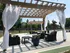 Charming outdoor patio with a wooden pergola, stylish wicker seating, and elegant white curtains, perfect for relaxation.
