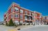 Modern red-brick apartment building with stylish balconies and landscaped entrance, set against a clear blue sky.