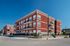 Elegant red-brick apartment building with modern balconies and lush landscaping on a sunny day.