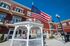 Charming apartment building with stylish red exterior, featuring white balconies, cozy gazebo, American flag, and bright outdoor space under a clear blue sky.