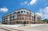 Modern apartment complex with stylish balconies, red brick facade, and ample parking under a clear blue sky.