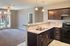 Bright and modern open kitchen layout with sleek countertops, dark wood cabinetry, and an inviting view into a cozy living area with plush carpeting and ample natural light.