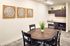 Charming dining nook with rustic wooden table, elegant wall art, and quaint kitchenette accentuated by lush greenery.