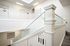 Elegant staircase with modern glass railing and ornate white wood balustrade in a well-lit apartment complex.