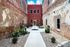 Charming brick courtyard featuring a modern red building, elegant benches, and lush greenery, offering a perfect blend of rustic and contemporary style.