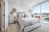 Bright and elegant bedroom with plush bed, modern decor, and expansive city view through floor-to-ceiling windows.