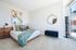 Bright, modern bedroom with stylish decor, featuring a cozy bed with colorful pillows, elegant wooden headboard, and artistic wall painting. Natural light streams in through a large window, highlighting the chic bookshelf and plush carpeting for a serene atmosphere.