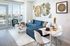 Bright and modern living room with a stylish blue sectional sofa, chic white furniture, and large windows offering a stunning city view.