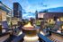 Luxurious rooftop patio with cozy fire pit, stylish seating, and panoramic cityscape backdrop at dusk.