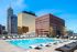 Luxurious rooftop pool area with modern lounge chairs, surrounded by a stunning city skyline under a clear blue sky.