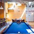 Bright loft-style apartment game room with a sleek blue pool table, stylish bar seating, and an elegant round dining table under modern pendant lighting.