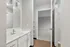 Bright modern bathroom with sleek white cabinets and a stylish sink, leading into a cozy carpeted bedroom through an open door.