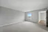 Bright and spacious bedroom featuring plush carpeting and a large window with a serene view, leading to an adjoining room with elegant wood flooring.