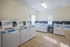 Modern laundry room featuring multiple top-loading washers and dryers with bright lighting and wood-style flooring.