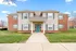 Charming two-story apartment building with red brick accents and a welcoming teal door, surrounded by lush greenery and a well-maintained lawn.