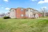 Beautiful two-story brick and siding apartment building surrounded by lush green lawns and clear blue skies.