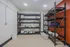 Contemporary storage room featuring sturdy black metal shelves and ample space for organization, enhanced by stylish lighting and a vibrant orange accent wall.