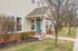 Charming townhouse exterior with brick accents and inviting green front door, set amidst manicured landscaping and mature trees.