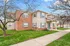 Charming two-story townhouse with red brick and beige siding, surrounded by lush grass and mature trees, offering a cozy suburban feel.