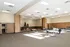 Spacious event hall with modern seating and festive Christmas decorations including tall, lit trees on a raised stage.