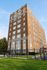 Majestic brick apartment building with classic architectural details, surrounded by lush green landscaping and a secure fence.