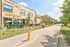 Charming urban building with a vibrant cafe featuring colorful umbrellas, adjacent to a scenic path lined with lush greenery.