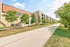 Modern apartment complex with stylish architecture, lush green trees, and a serene walkway under a bright blue sky.