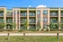 Modern apartment building with large windows and private balconies, surrounded by lush greenery and a scenic walkway.