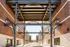 Modern architectural entrance with decorative metal beams and brick buildings, offering a welcoming pathway to a stylish community.