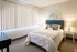 Bright and cozy bedroom with a plush blue headboard, elegant bedside tables, and modern decor, featuring natural light filtering through large vertical blinds.