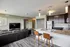 Modern open-concept living space featuring a sleek kitchen with granite countertops, stylish dark cabinetry, and a bright living area with a large TV and leather seating.