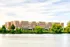 Charming brick apartment complex by the serene riverside, surrounded by lush greenery and clear skies.