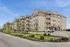 Modern apartment complex with four-story buildings, balconies, and landscaped surroundings under a bright blue sky.