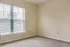 Bright, sunlit room with plush carpet flooring and large window with blinds, perfect for a cozy bedroom or home office.